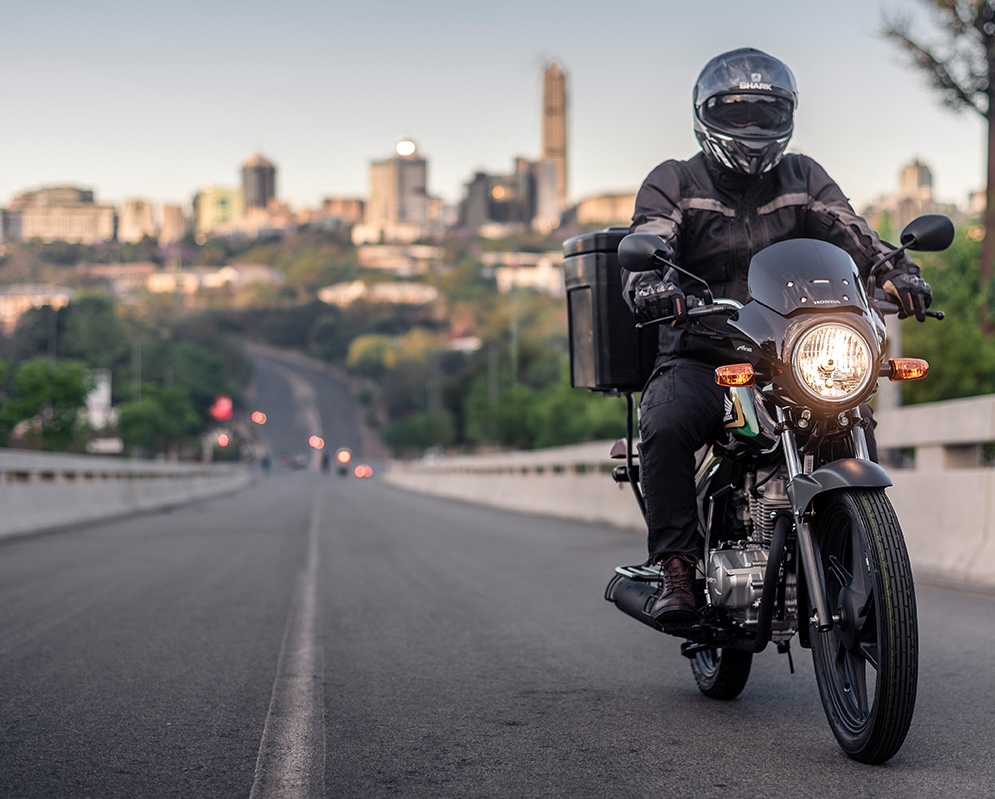 Delivery rider on a Honda Ace crossing a Johannesburg highway at dusk